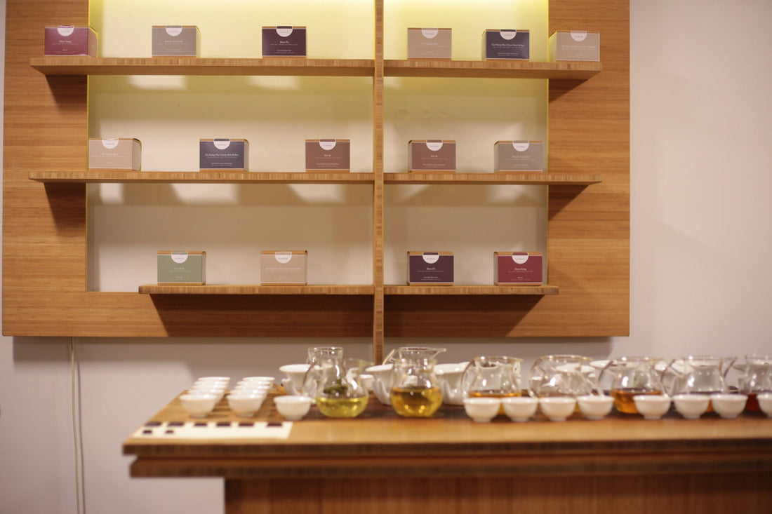 Shelves of packaged tea boxes above a long tasting table with rows of tea cups.