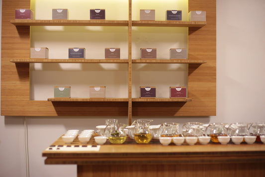 Shelves of packaged tea boxes above a long tasting table with rows of tea cups.