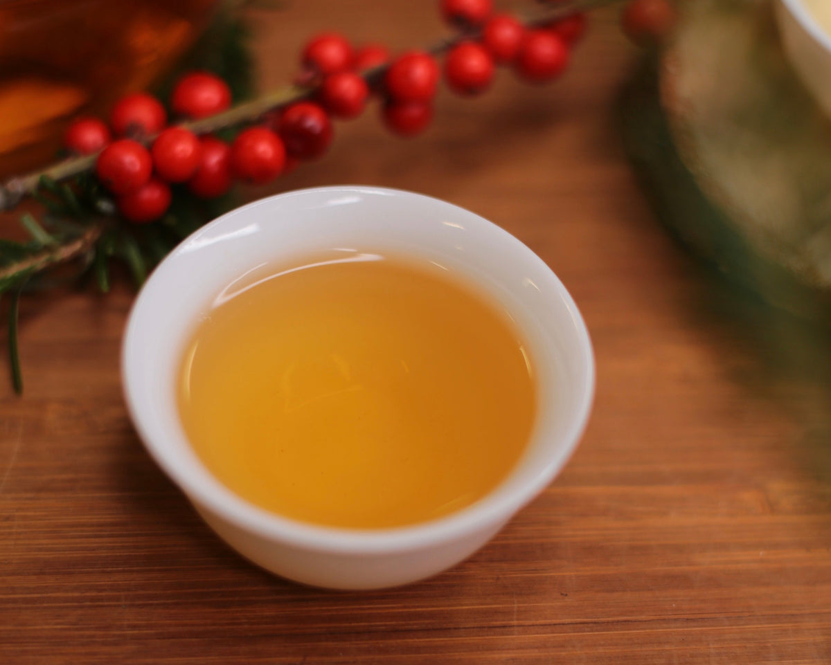 A small white cup of amber tea beside red winter berries on a wooden table.