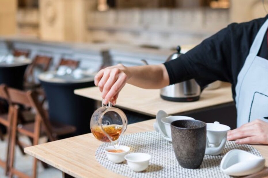 Tea being poured from a glass pitcher into small cups at a tea bar counter