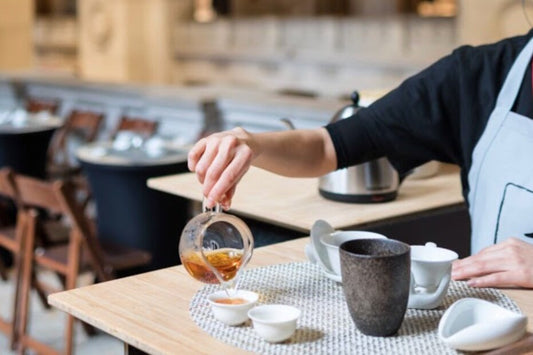 Tea being poured from a glass pitcher into small cups at a tea bar counter