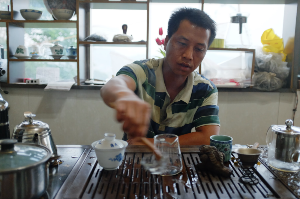 Man pouring hot water over a gai wan and glass pitcher during a gong fu tea brewing session