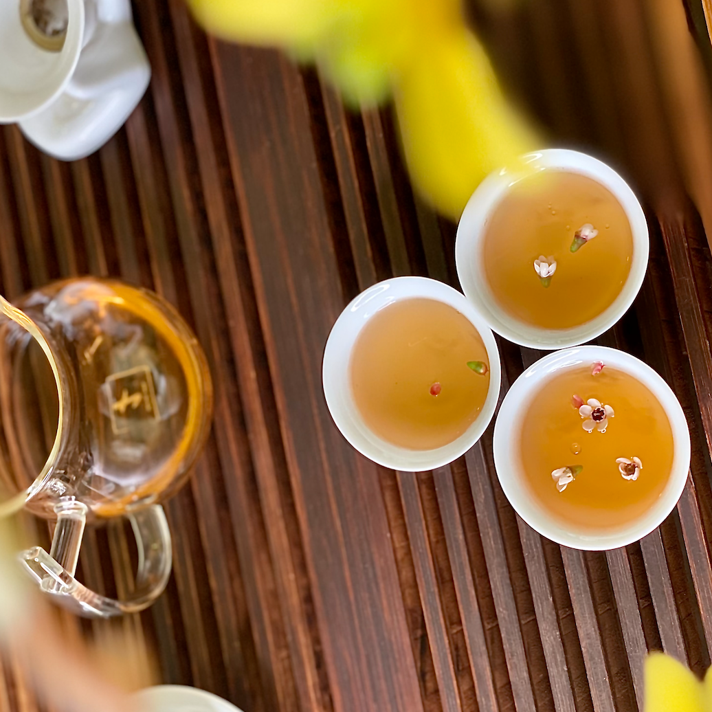 Overhead view of three cups of amber tea garnished with small flower petals