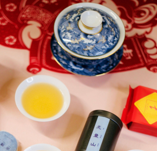 A blue-and-white gaiwan, cup of golden tea, and tea tin on a red Chinese New Year tablecloth.