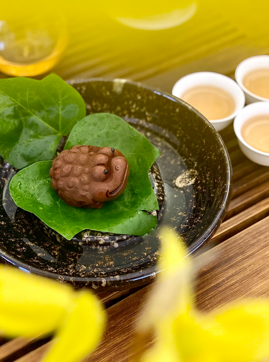 Clay hedgehog-shaped tea pet resting on a leaf beside cups of brewed tea