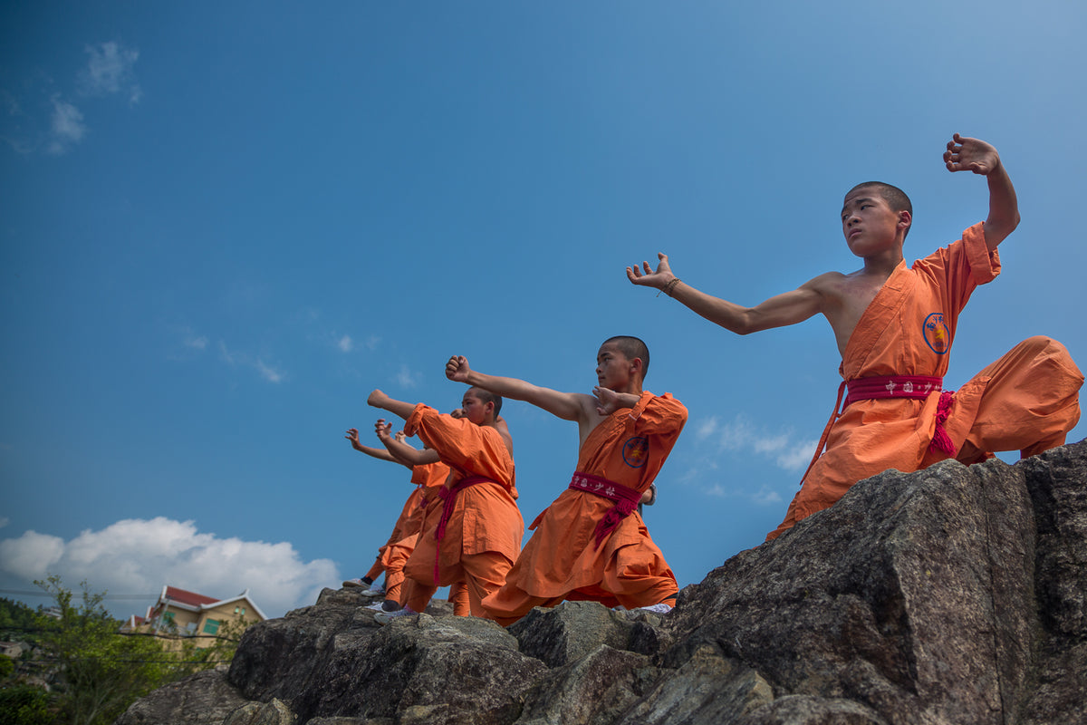 Traditional performers in orange robes on a rocky landscape.